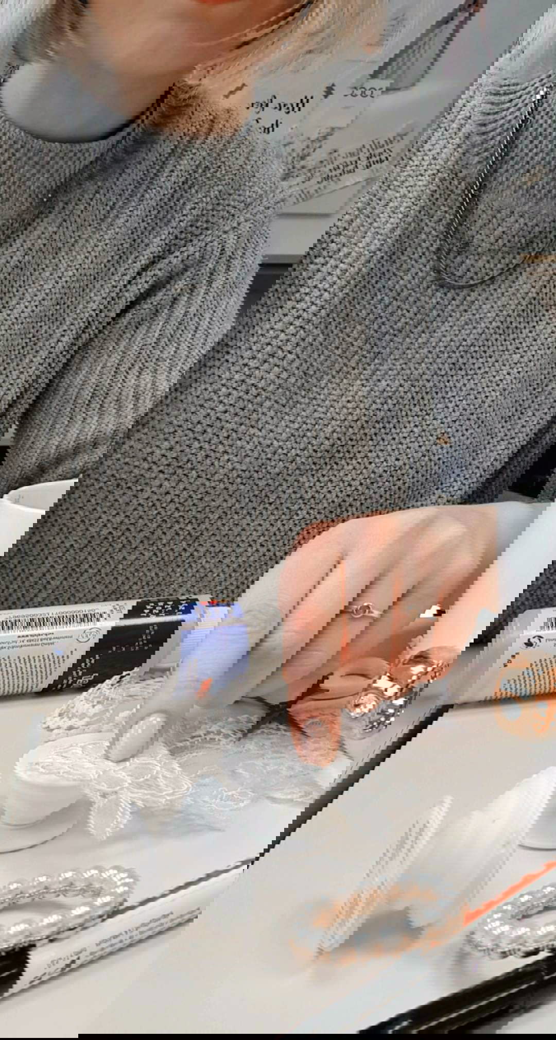 Eine Frau in einem Strickpullover arbeitet an einem Popsocket-DIY-Projekt und verwendet Spitze zur Verzierung. Weitere Bastelmaterialien wie Kleber und Perlen sind daneben arrangiert.