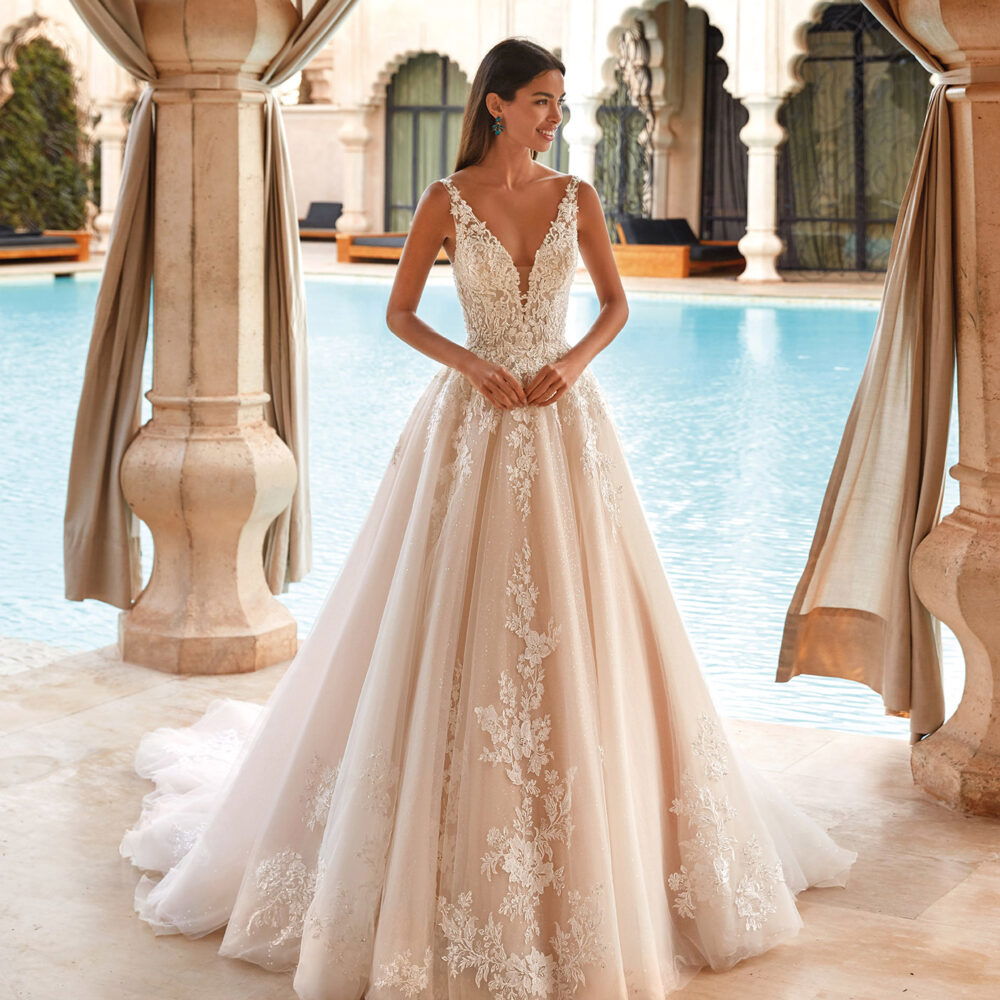 Braut in einem wunderschönen Tüllkleid mit Spitzendetails und V-Ausschnitt, posierend vor einem Pool in luxuriösem Ambiente.