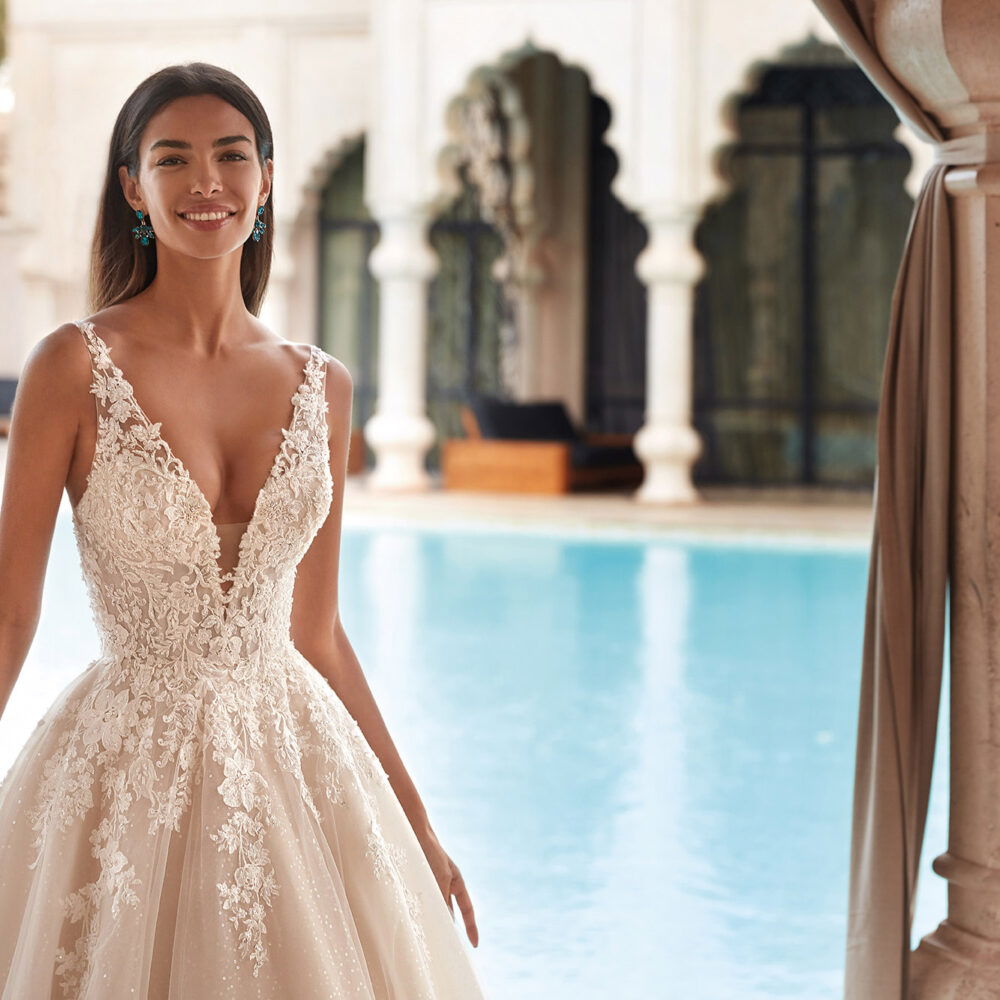 Romantisches Brautkleid mit floralen Details und V-Ausschnitt, getragen von einer Braut vor einem luxuriösen Pool.