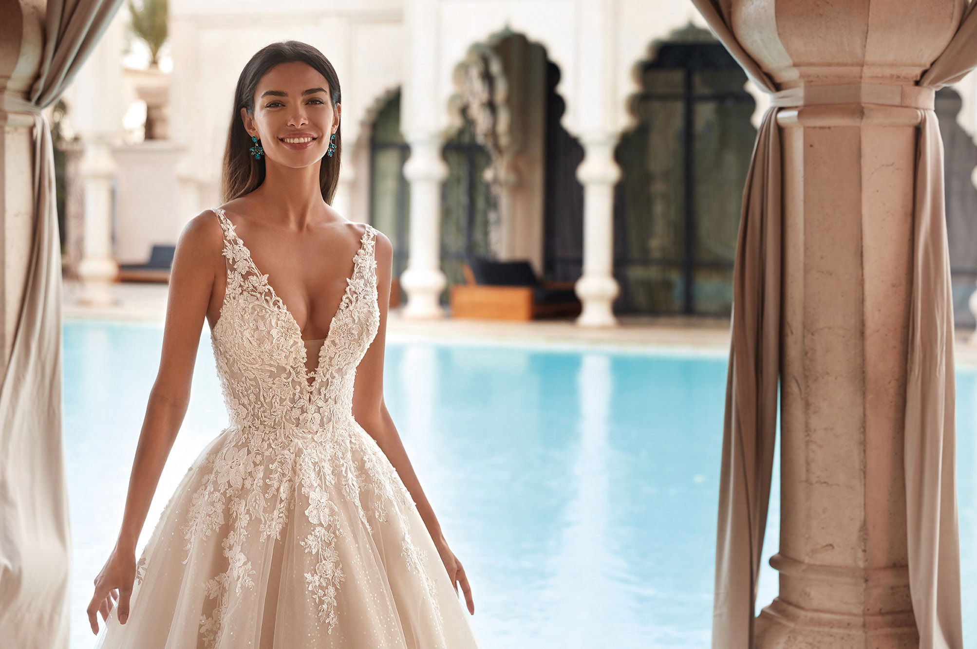 Romantisches Brautkleid mit floralen Details und V-Ausschnitt, getragen von einer Braut vor einem luxuriösen Pool.