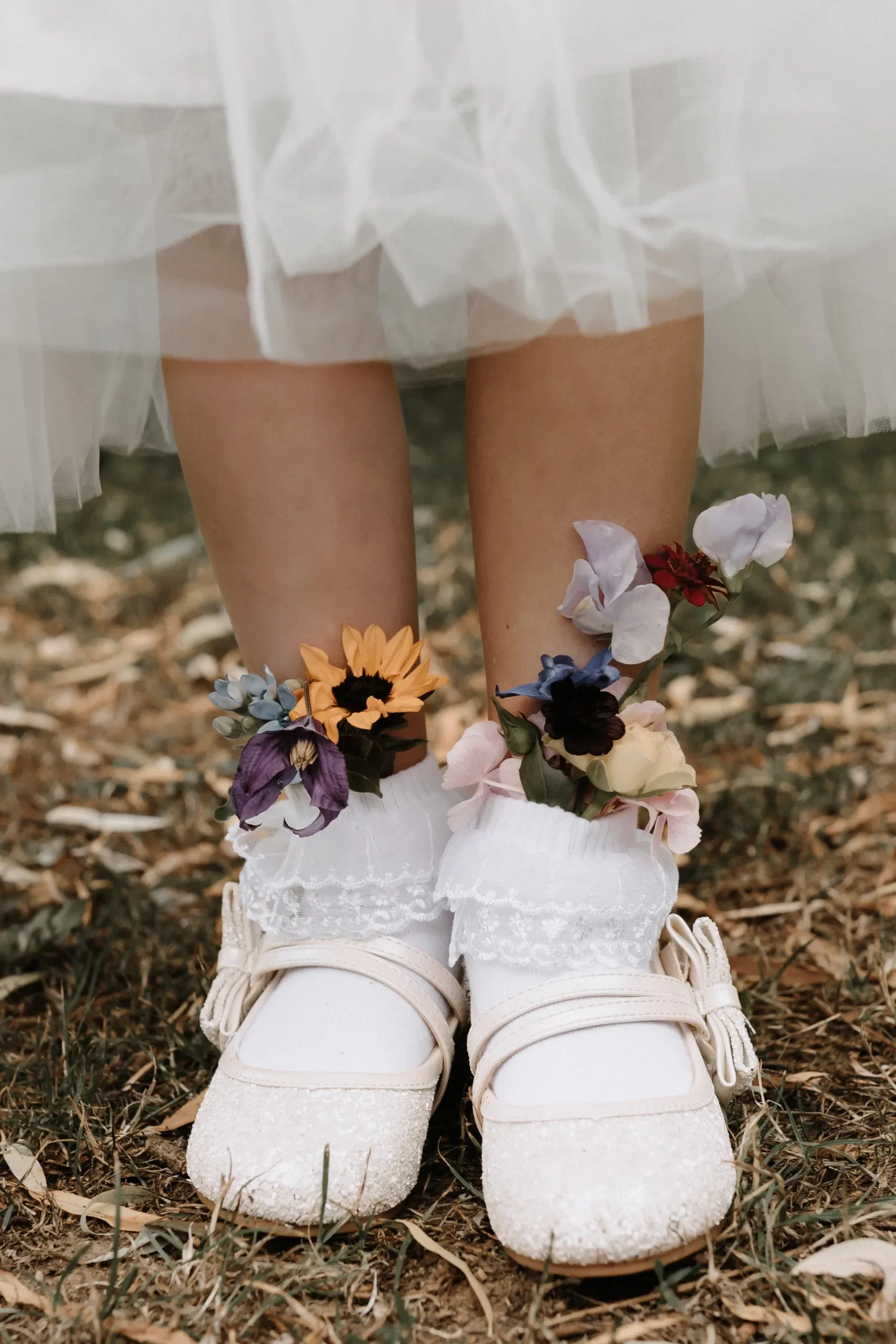 Detailaufnahme von Mädchenschuhen bei einer Hochzeit, verziert mit farbenfrohen Blüten und weißen Spitzen-Socken.