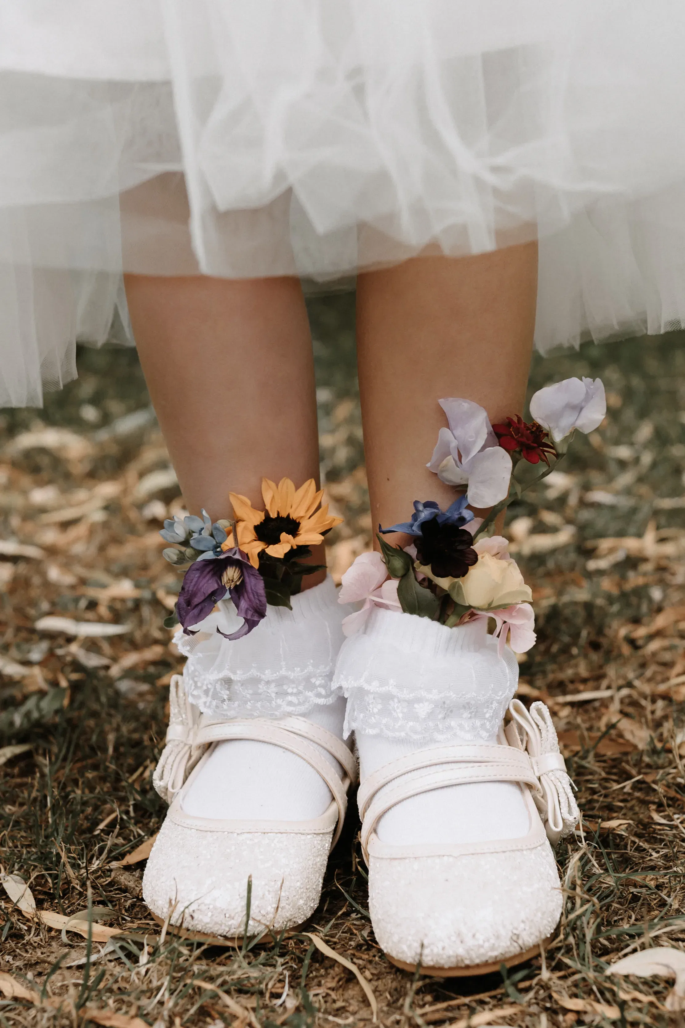 Detailaufnahme von Mädchenschuhen bei einer Hochzeit, verziert mit farbenfrohen Blüten und weißen Spitzen-Socken.