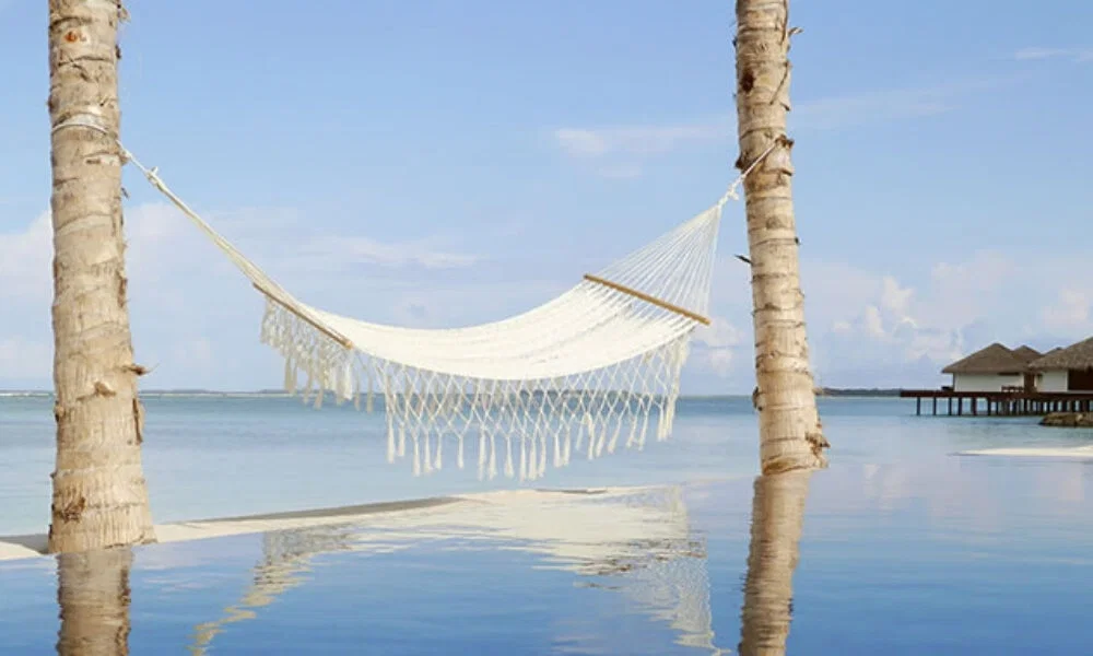 Traumhafte Hängematte über einem Infinity Pool, von Palmen gehalten, mit weitem Blick auf den türkisfarbenen Ozean und Wasservillen.