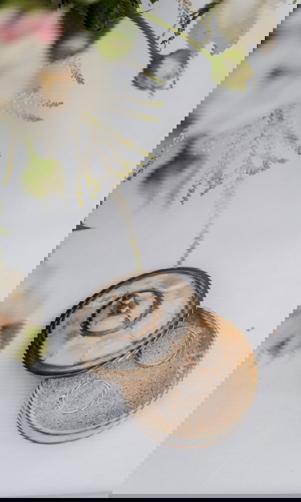 Offenes Schmuckkästchen mit Muschel- und Perlmutt-Muster, gefüllt mit Sand, auf dem die Eheringe liebevoll präsentiert sind.