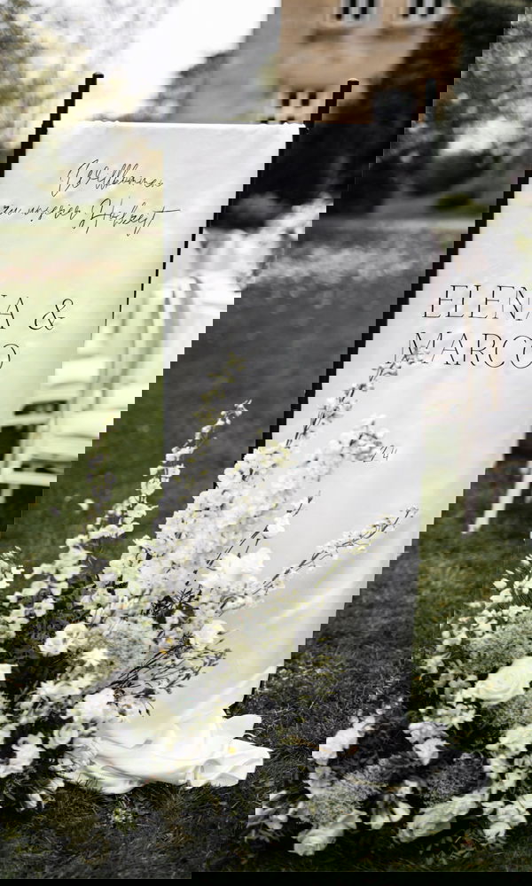 Ein Willkommensschild mit den Namen „Elena & Marco“ sowie weißen Blumenarrangements lädt die Gäste zur Hochzeitsfeier im Freien ein.