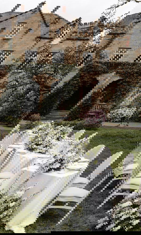 Romantische Outdoor-Tafel mit weißen Blumen und gedeckten Stühlen, stilvoll arrangiert im Garten einer historischen Villa.