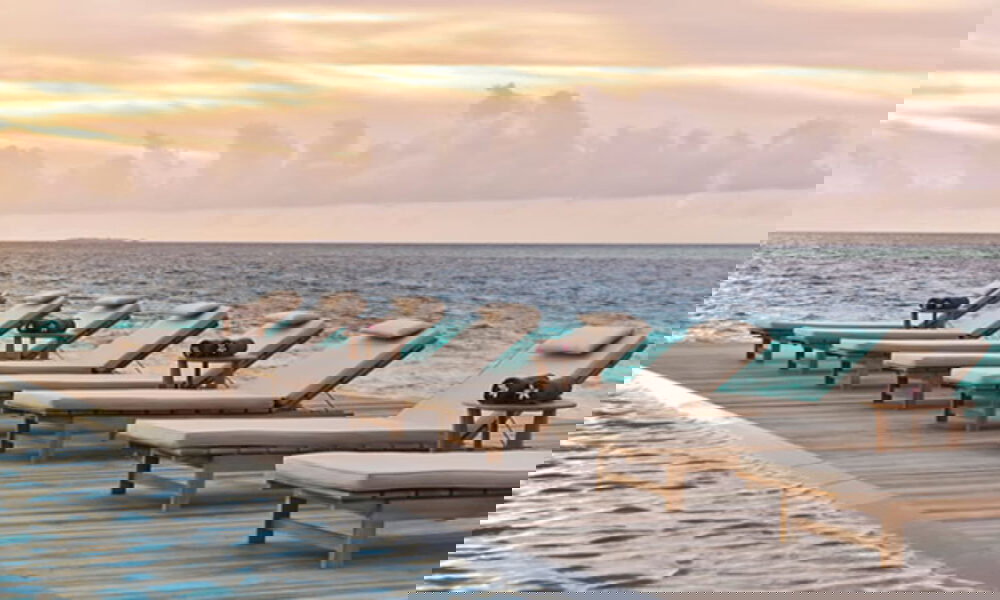 Reihe von Liegen am Poolrand mit direktem Meerblick, perfekt für entspannte Momente bei Sonnenuntergang auf den Malediven.