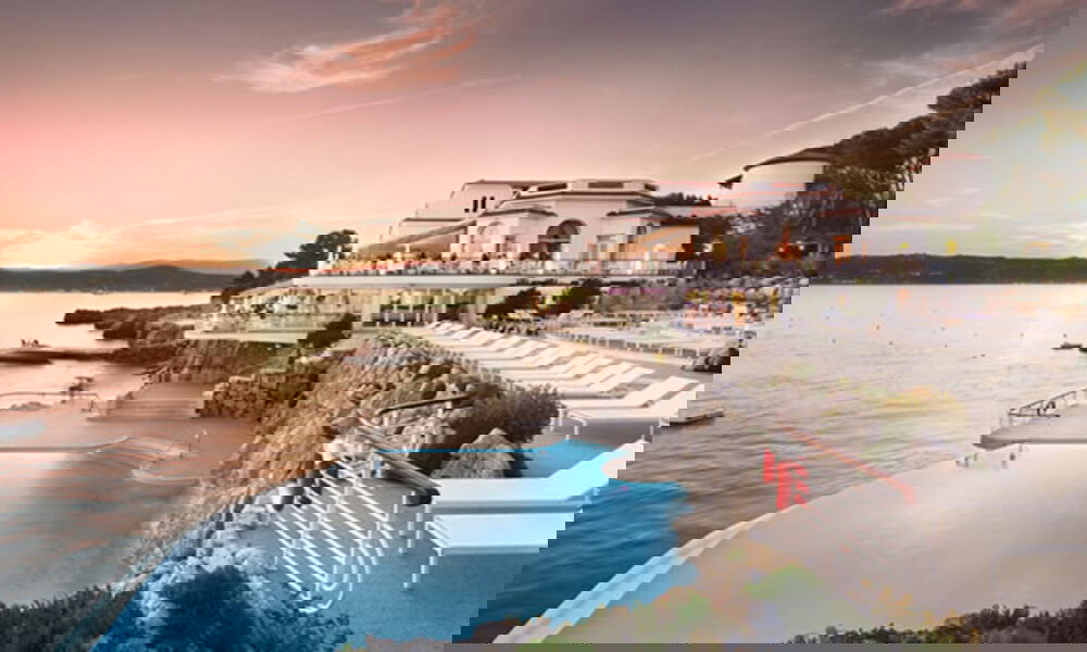 Eleganter Pool in Südfrankreich, eingebettet in Felsen und mit Blick auf das Meer, umgeben von Liegen und einem mediterranen Hotel bei Dämmerung.