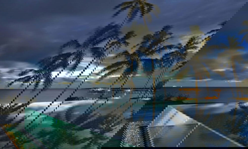 Luxuriöser Infinity Pool bei Nacht in Sansibar, umgeben von Palmen, mit ruhigem Meer und einer dramatischen, bewölkten Himmelskulisse.