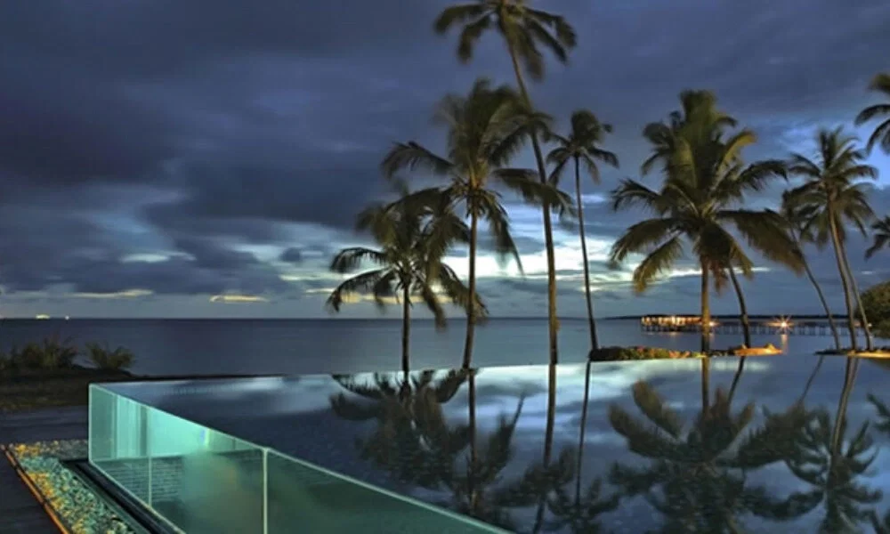Luxuriöser Infinity Pool bei Nacht in Sansibar, umgeben von Palmen, mit ruhigem Meer und einer dramatischen, bewölkten Himmelskulisse.
