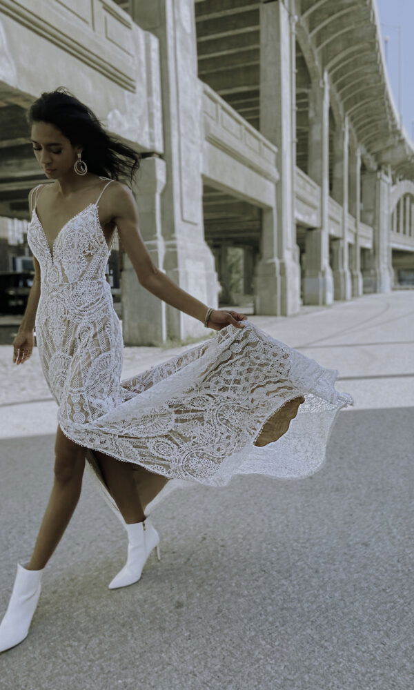 Boho-Braut in einem fließenden Spitzenkleid und weißen Stiefeletten, die dynamisch in einer urbanen Umgebung posiert.