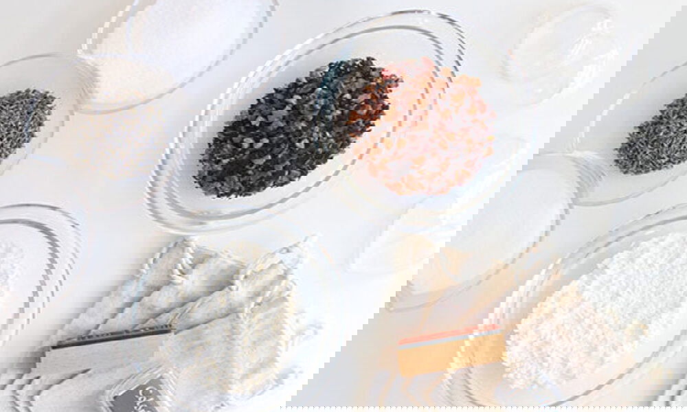 Verschiedene Zutaten und Materialien zur Herstellung von Badekugeln: getrocknete Blüten, Pulverzutaten, Stoffbeutel sowie Stempel und Stempelkissen für die Verpackung.