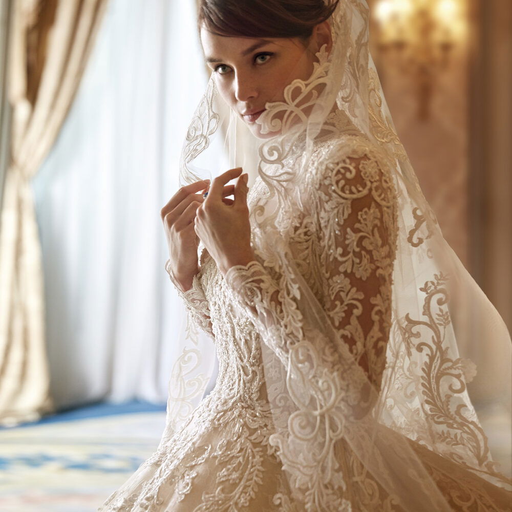 Romantischer Braut-Look mit Spitzenkleid und Schleier, der das Gesicht umspielt, ideal für eine elegante und stilvolle Hochzeit.