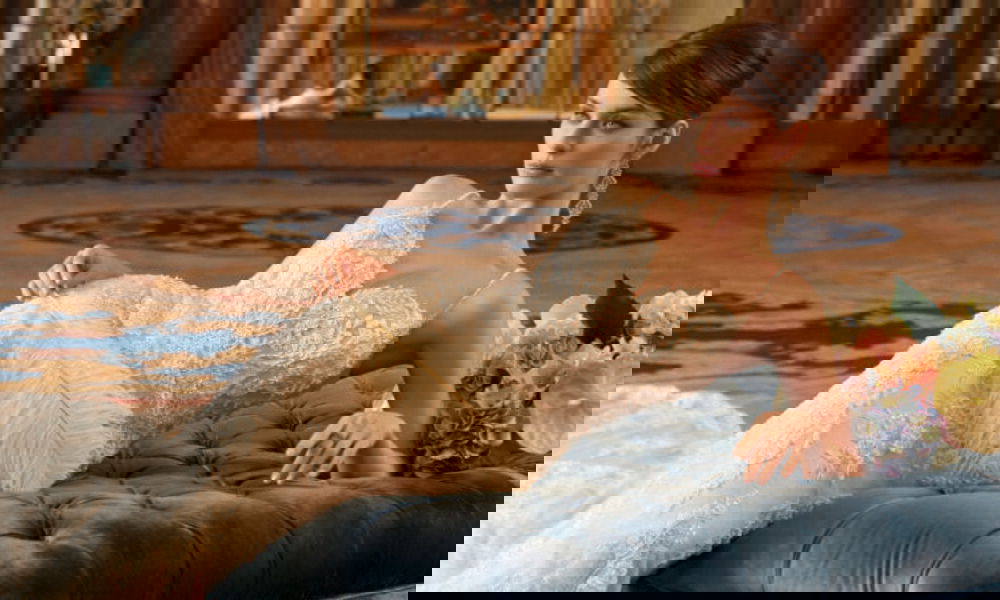 Romantisches Spitzen-Brautkleid mit schmalen Trägern und aufwendigen Stickereien, präsentiert in einem eleganten Raum auf einer Couch.