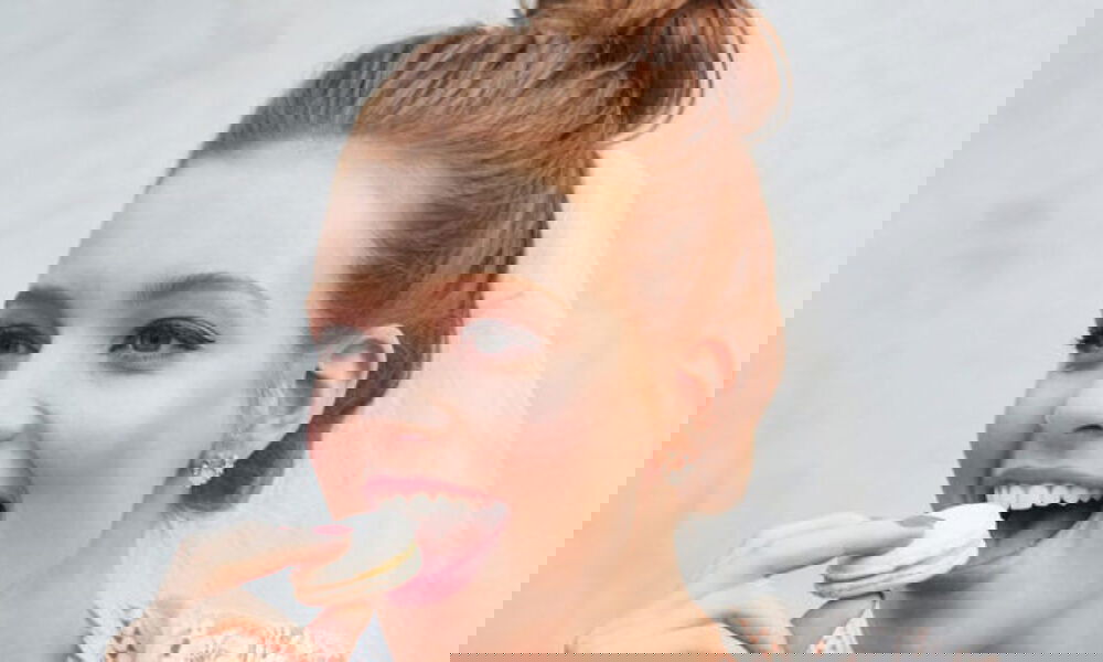 Junge Braut in festlicher Stimmung, mit frischem Hochzeits-Look, genießt einen Macaron und zeigt pure Freude.