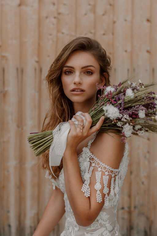 Nahaufnahme einer Boho-Braut mit einem Blumenstrauß aus getrockneten Blüten. Ihr Haar ist offen und leicht gewellt, passend zu ihrem lässigen Look.