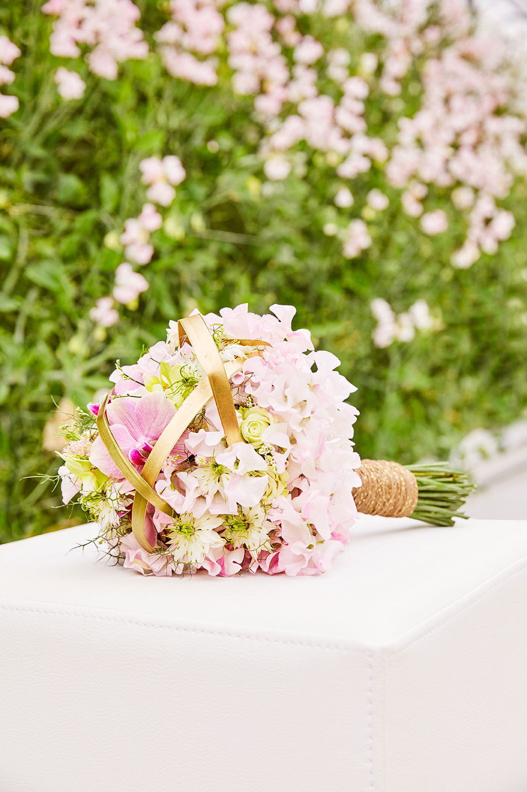 Ein romantischer Brautstrauß in Rosa und Creme mit goldenen Akzenten, ruht auf einem weißen Tisch und strahlt Eleganz aus.
