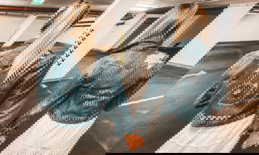 Zwei Frauen in personalisierten Jeansjacken im Parkhaus. Die linke Jacke trägt ein freches Motiv mit "forever" darunter, und die rechte Jacke ist mit "very important bride" und funkelnden Details verziert.