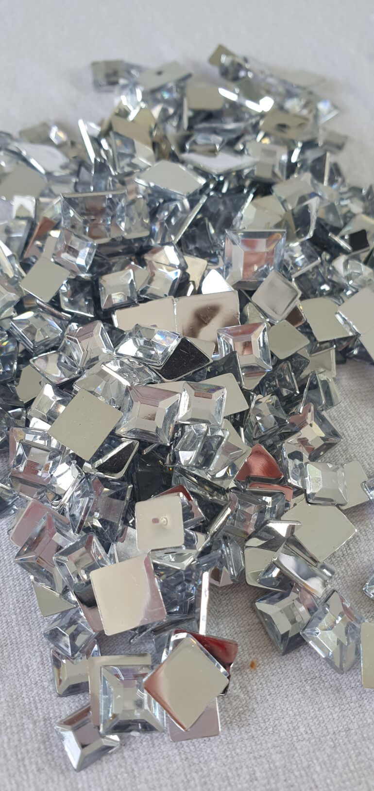 Eine Sammlung silberner Glitzersteine in einer Nahaufnahme. Die Steine haben quadratische und rechteckige Formen und glitzern im Licht.