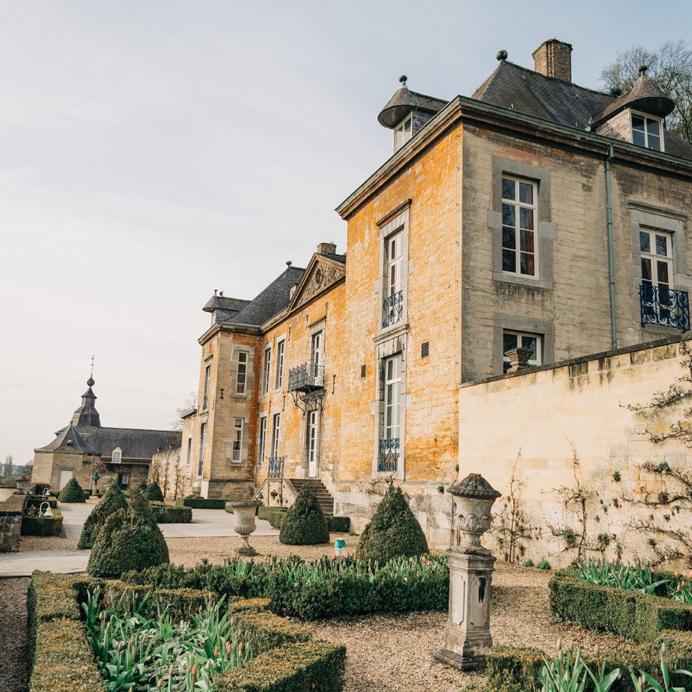 Ein prachtvolles Herrenhaus aus hellem Stein mit barockem Garten, dekoriert mit Buchsbaumhecken und Skulpturen, im Licht der Abendsonne.