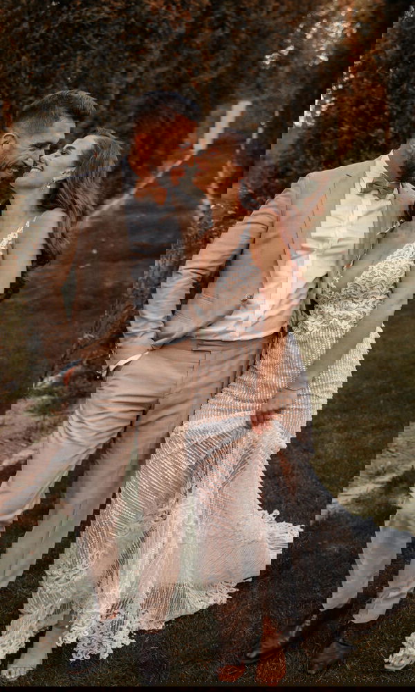 Braut und Bräutigam genießen einen intimen Moment im Grünen; sie trägt ein Spitzenkleid, er einen klassischen beigen Anzug.