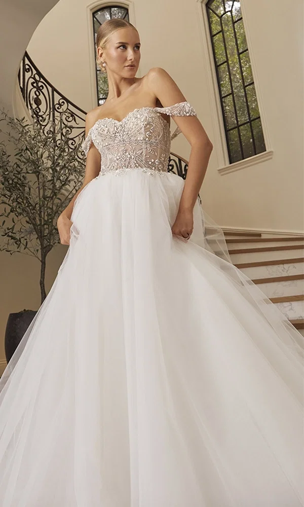 Braut in einem trägerlosen Hochzeitskleid mit floralen Stickereien und langer Schleppe, posiert elegant vor einem Hintergrund aus grünen Bäumen und einem kleinen Teich.