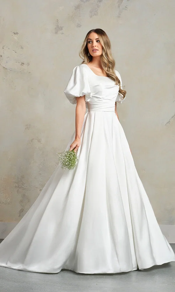 Braut in einem prachtvollen Ballkleid-Hochzeitskleid mit aufwendig verzierten Spitzen-Details und langer Schleppe, steht in einer luxuriösen Villa mit hohen Fenstern.