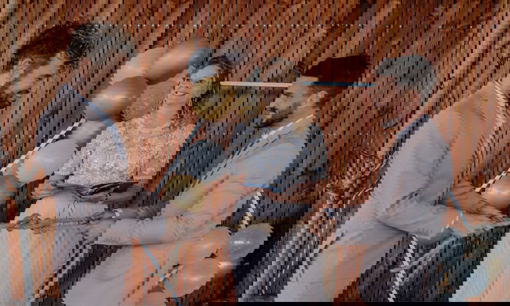 Hochzeitspaar mit Seil in den Händen als Teil ihrer Trauzeremonie, beide lachen, während die Rednerin das Ritual begleitet.