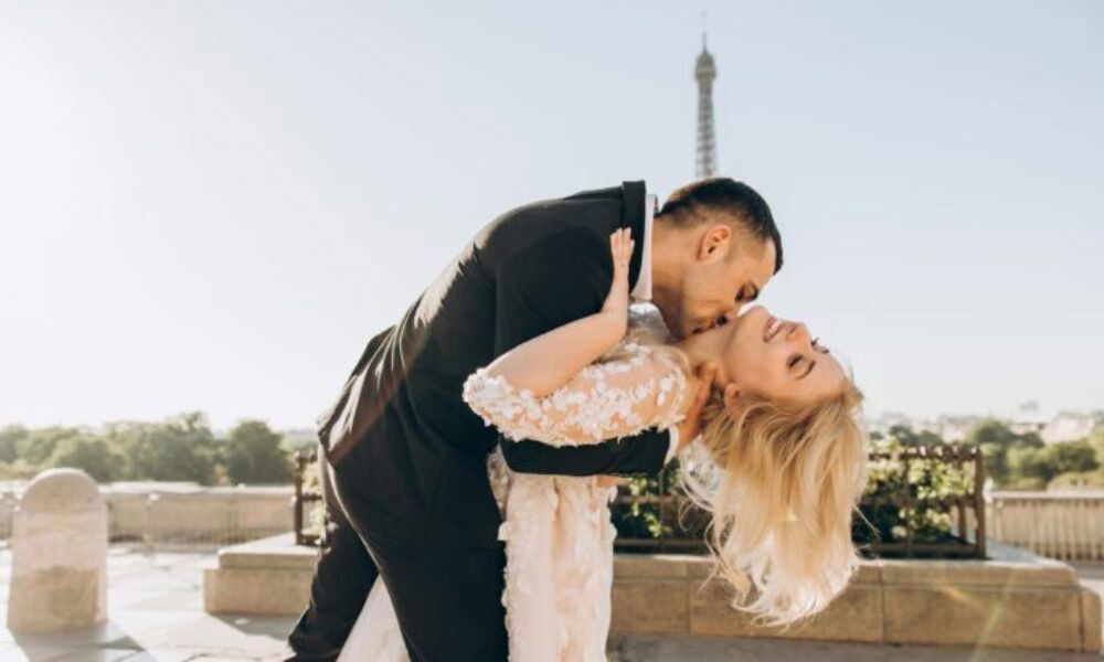 Elegantes Hochzeitsfoto: Ein frisch verheiratetes Paar genießt einen innigen Moment vor dem Eiffelturm, während der Bräutigam seine Braut hält.