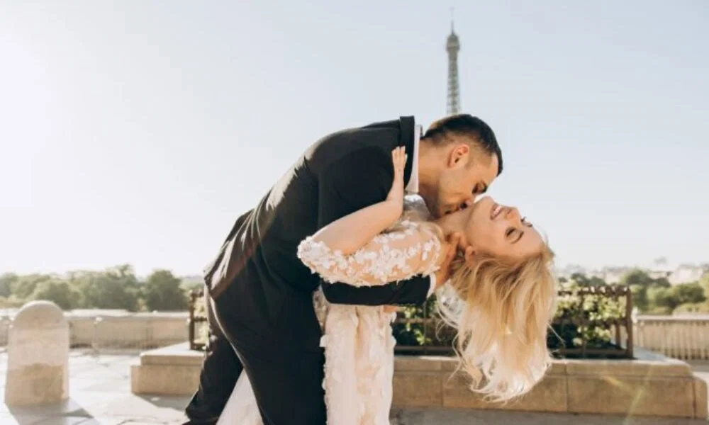 Elegantes Hochzeitsfoto: Ein frisch verheiratetes Paar genießt einen innigen Moment vor dem Eiffelturm, während der Bräutigam seine Braut hält.