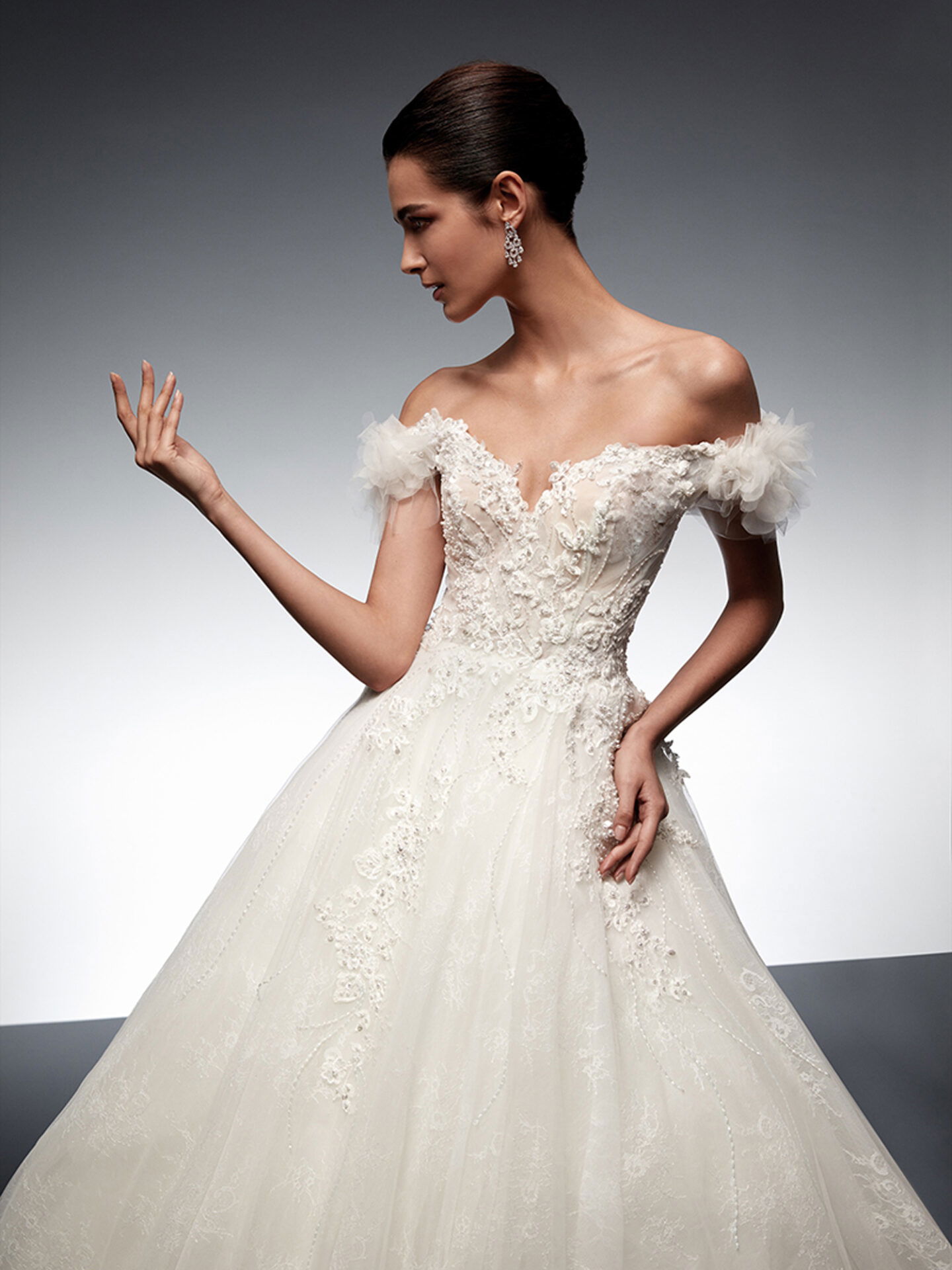 Eine Braut trägt ein schulterfreies, glitzerndes Tüllkleid mit aufwendigen Perlendetails, das eine romantische Atmosphäre verbreitet.