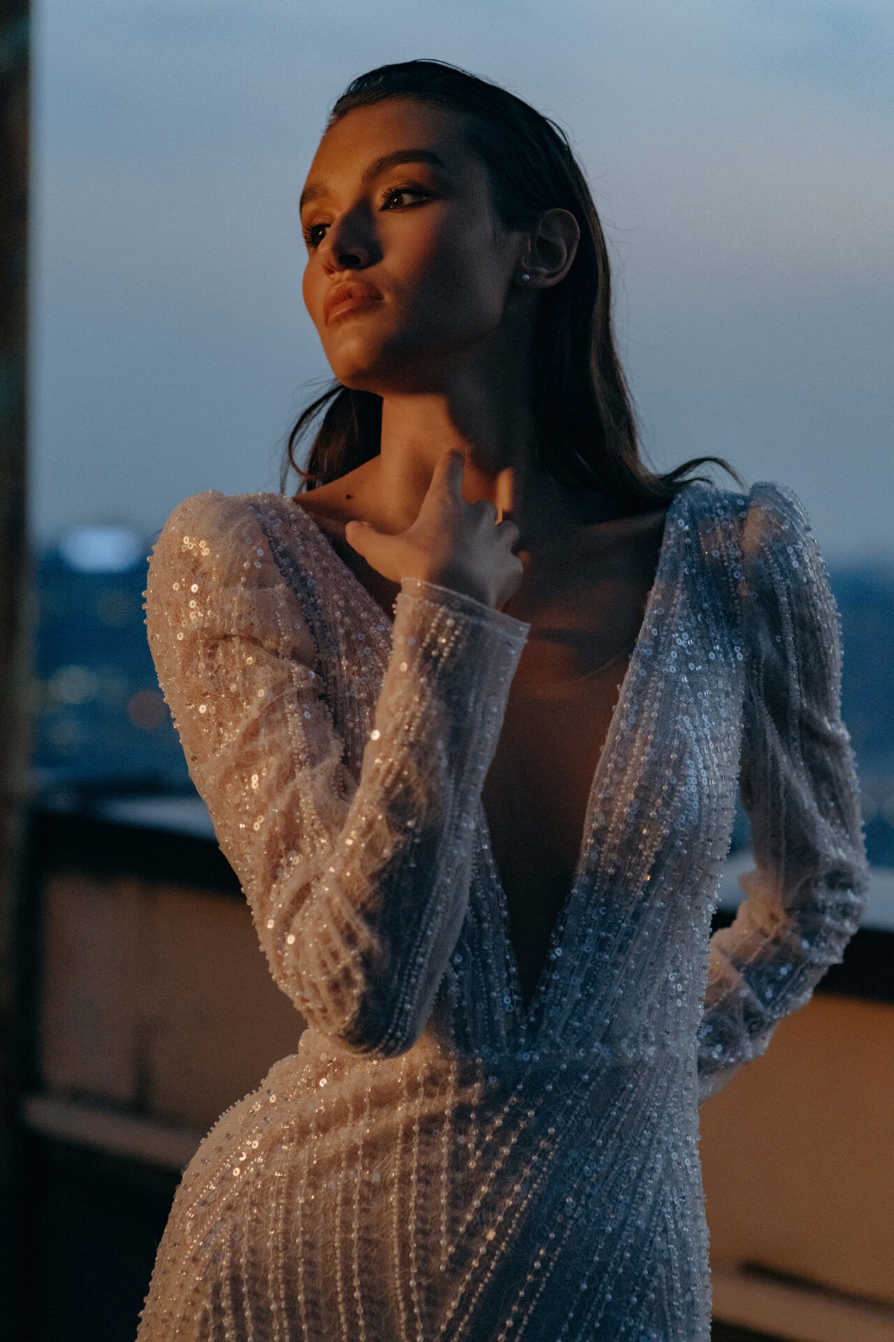 Eine Braut in einem funkelnden Kleid, bedeckt mit Pailletten und langen Ärmeln, genießt die Abenddämmerung, während sie für die Kamera posiert.