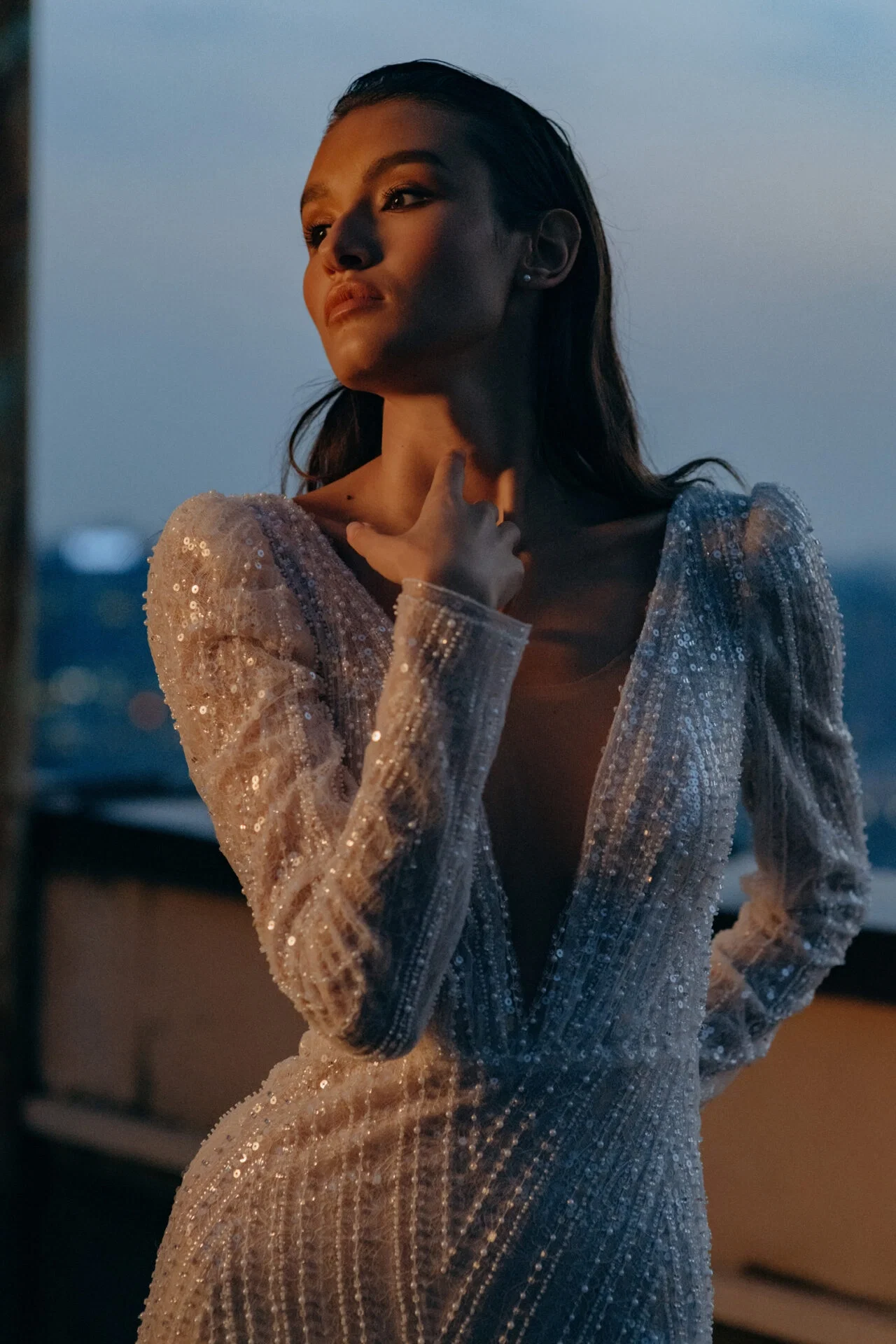 Eine Braut in einem funkelnden Kleid, bedeckt mit Pailletten und langen Ärmeln, genießt die Abenddämmerung, während sie für die Kamera posiert.