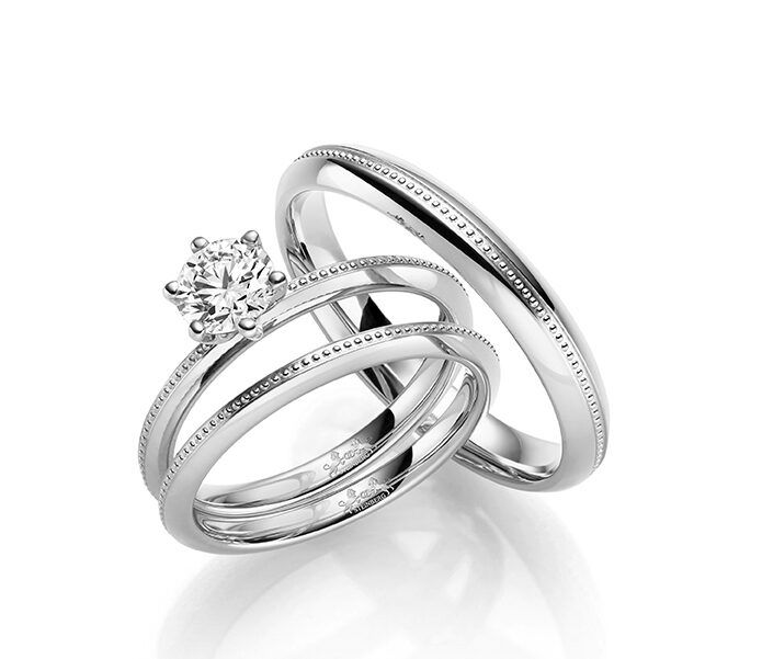 Eheringe aus glänzendem Weißgold, ein Ring mit einem funkelnden Solitär-Diamanten und der andere schlicht gehalten. Die Ringe zeichnen sich durch ihre schlichte Eleganz und filigranen Kanten aus.