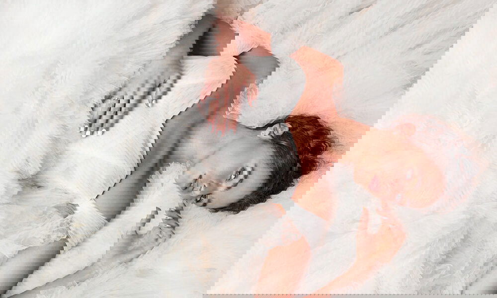 Braut in einem üppigen Tüllkleid, liegend, mit verträumtem Ausdruck. Das Kleid ist schulterfrei und betont die romantische Atmosphäre.