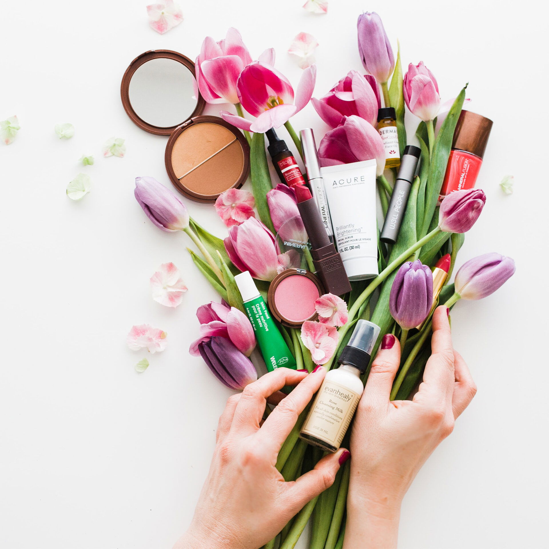 Beauty-Produkte, darunter Lippenstift, Foundation und Puder, arrangiert zwischen zarten Tulpenblüten – perfekt für den Brautlook im Frühling.