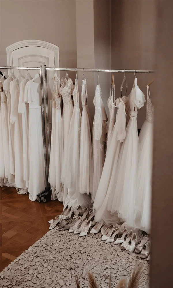 weiße Brautkleider in unterschiedlichen Stilen hängen an einer Kleiderstange, davor weiße Brautschuhe aufgereiht