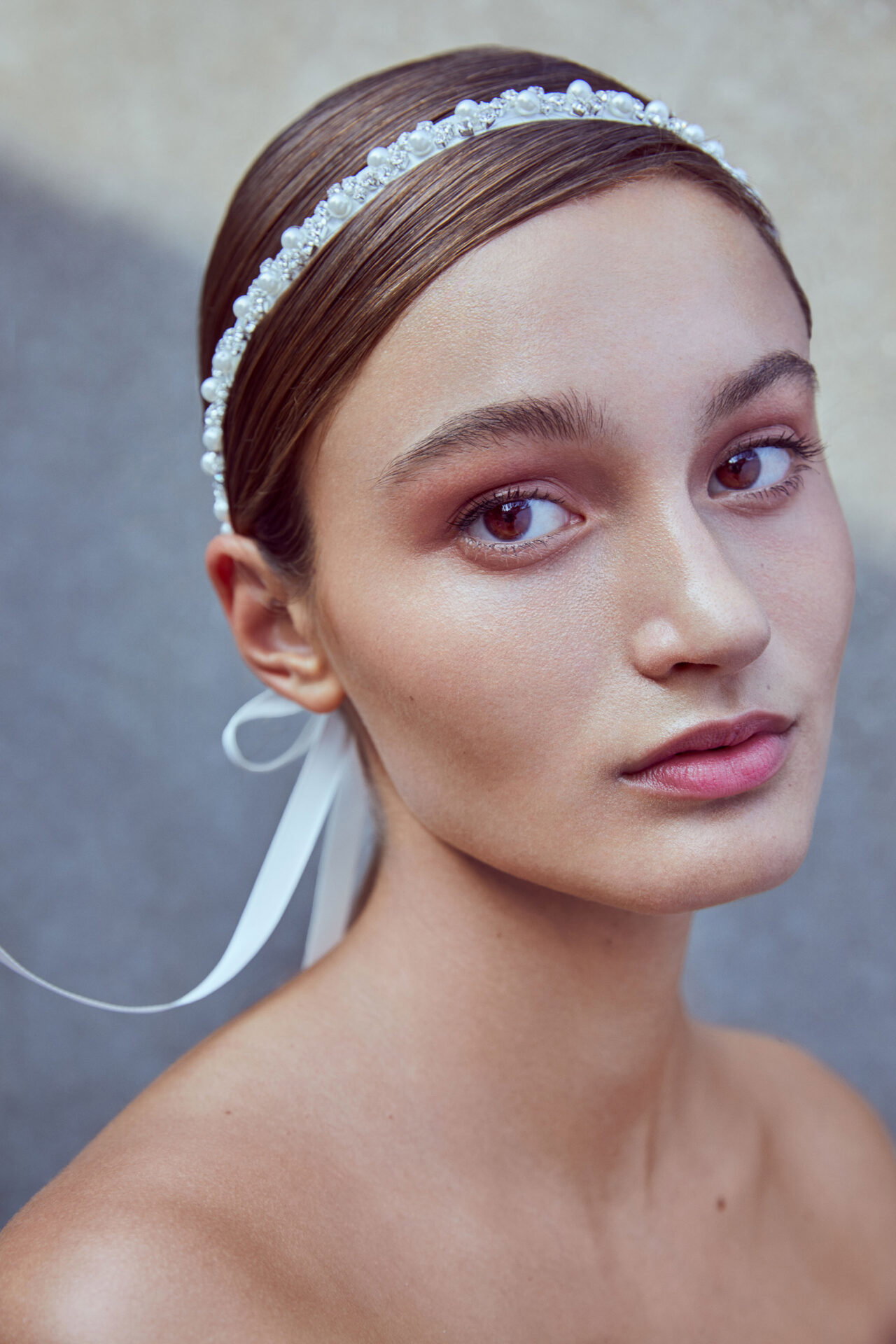 Junge Frau mit minimalistischer Frisur und einem eleganten, mit Perlen besetzten Haarband. Das natürliche Make-up verleiht ihr einen sanften Glanz.