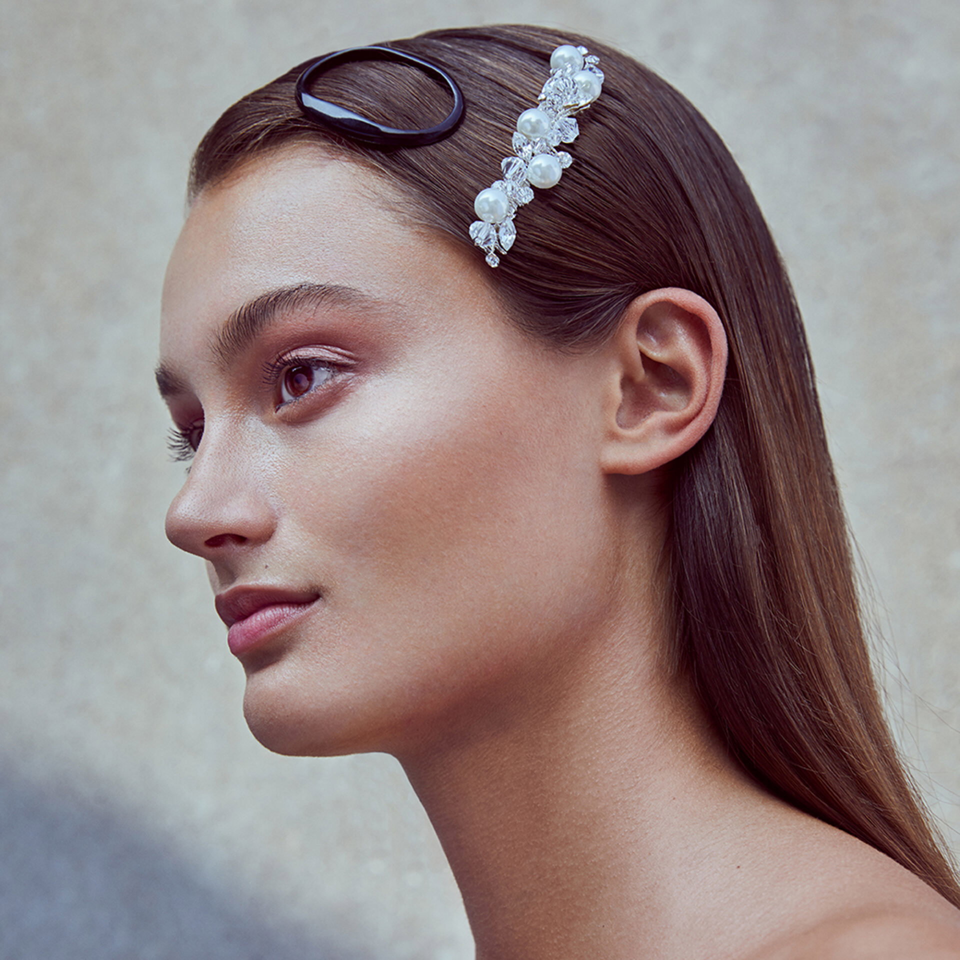 Model mit glattem, braunem Haar und einem Haarschmuck aus Perlen und Steinen. Ihr dezentes Make-up unterstreicht den eleganten, schlichten Stil.