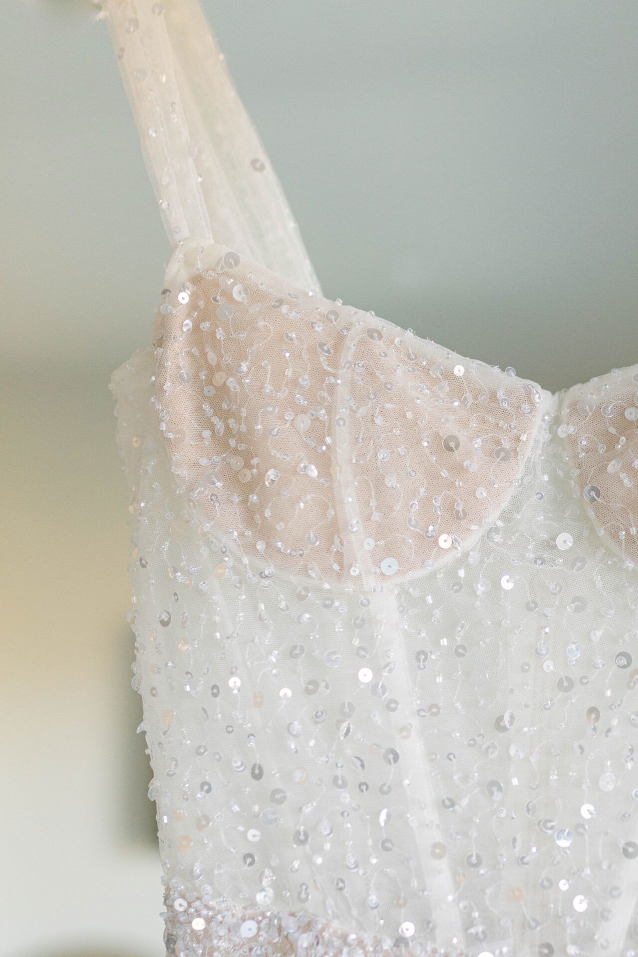 Nahaufnahme des Oberteils eines glitzernden Brautkleids mit durchsichtigen Trägern und funkelnden Pailletten, die das Kleid zum Strahlen bringen.