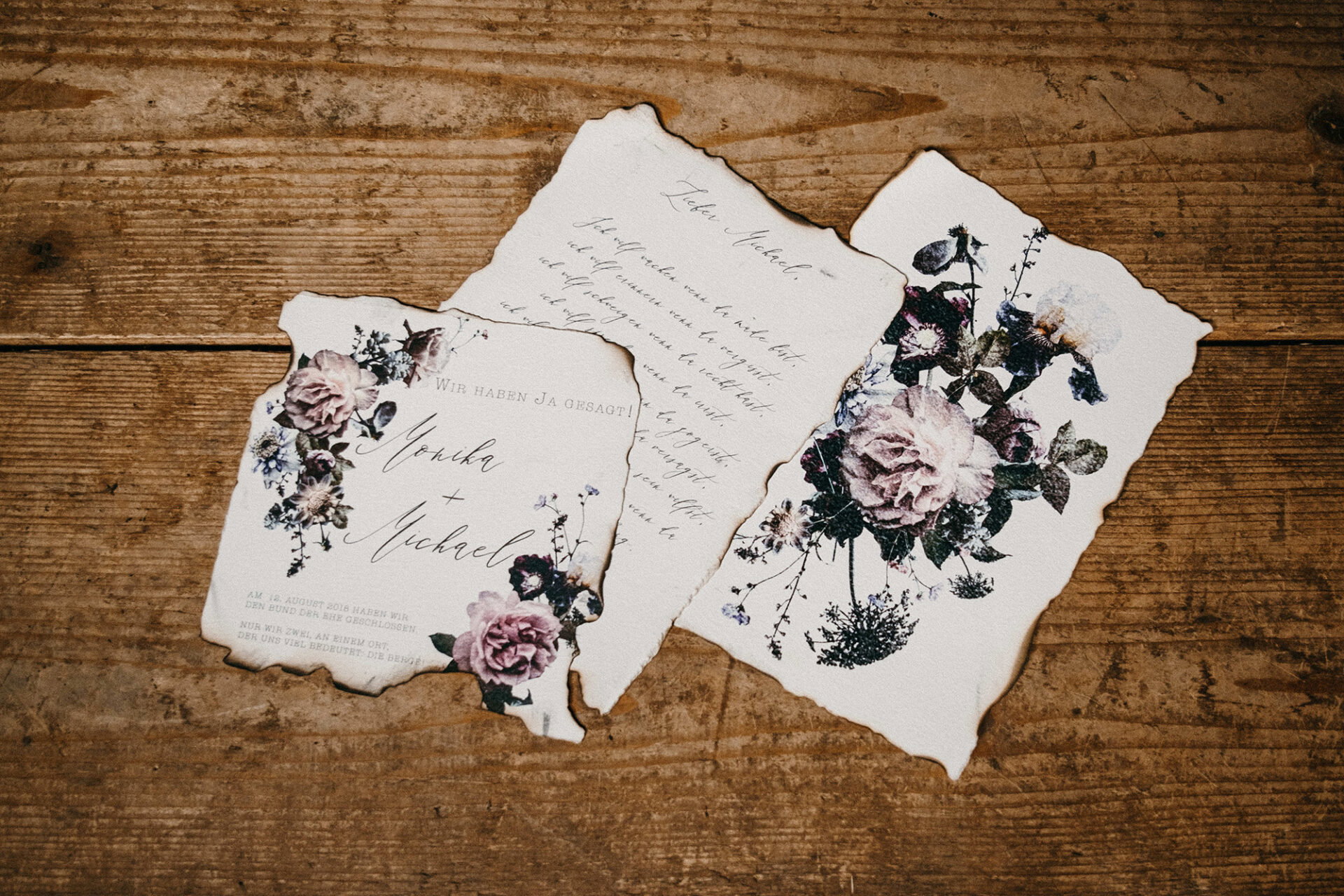 Hochzeitseinladungen im Landhausstil, verziert mit Blumendekor und Handlettering auf Pergamentpapier mit antik angehauchten, verbrannten Rändern.