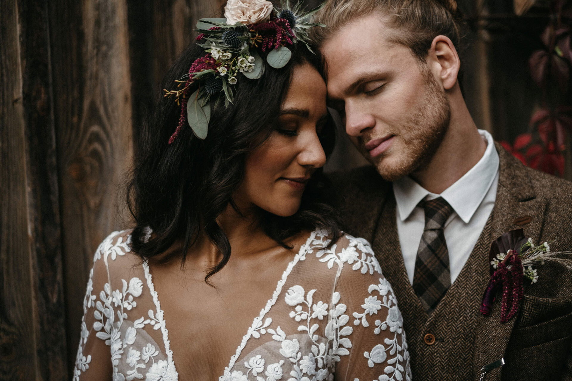 Intimer Moment zwischen Braut und Bräutigam, sie trägt einen Blumenkranz aus Eukalyptus und dunklen Beeren, er ist in einen eleganten Tweedanzug gekleidet.