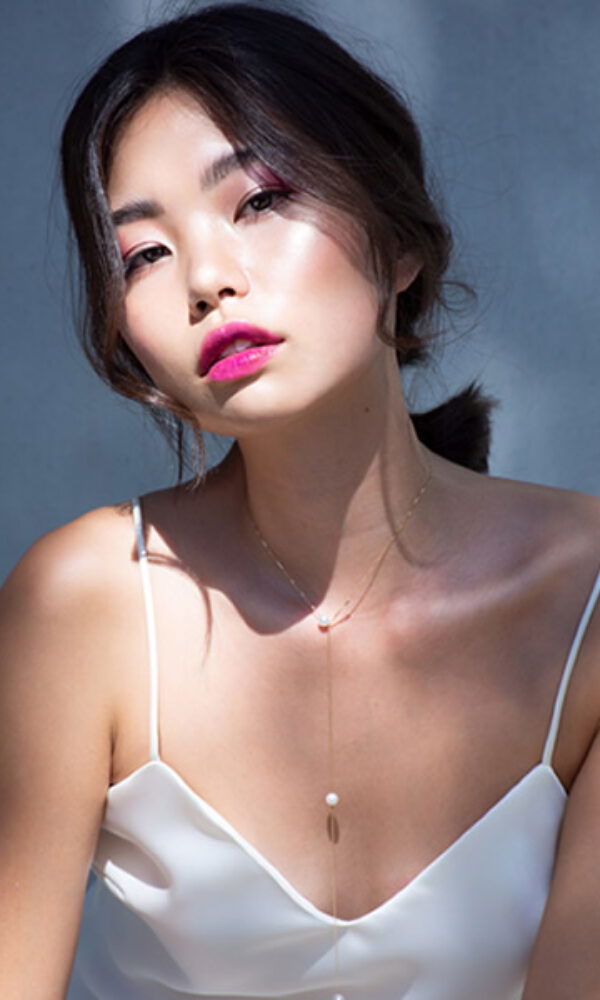 Porträt einer Frau in einem eleganten, weißen Spaghettiträger-Top. Ihr Look wird durch strahlenden Lippenstift und eine locker gebundene Hochsteckfrisur betont.