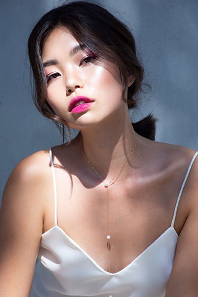 Porträt einer Frau in einem eleganten, weißen Spaghettiträger-Top. Ihr Look wird durch strahlenden Lippenstift und eine locker gebundene Hochsteckfrisur betont.