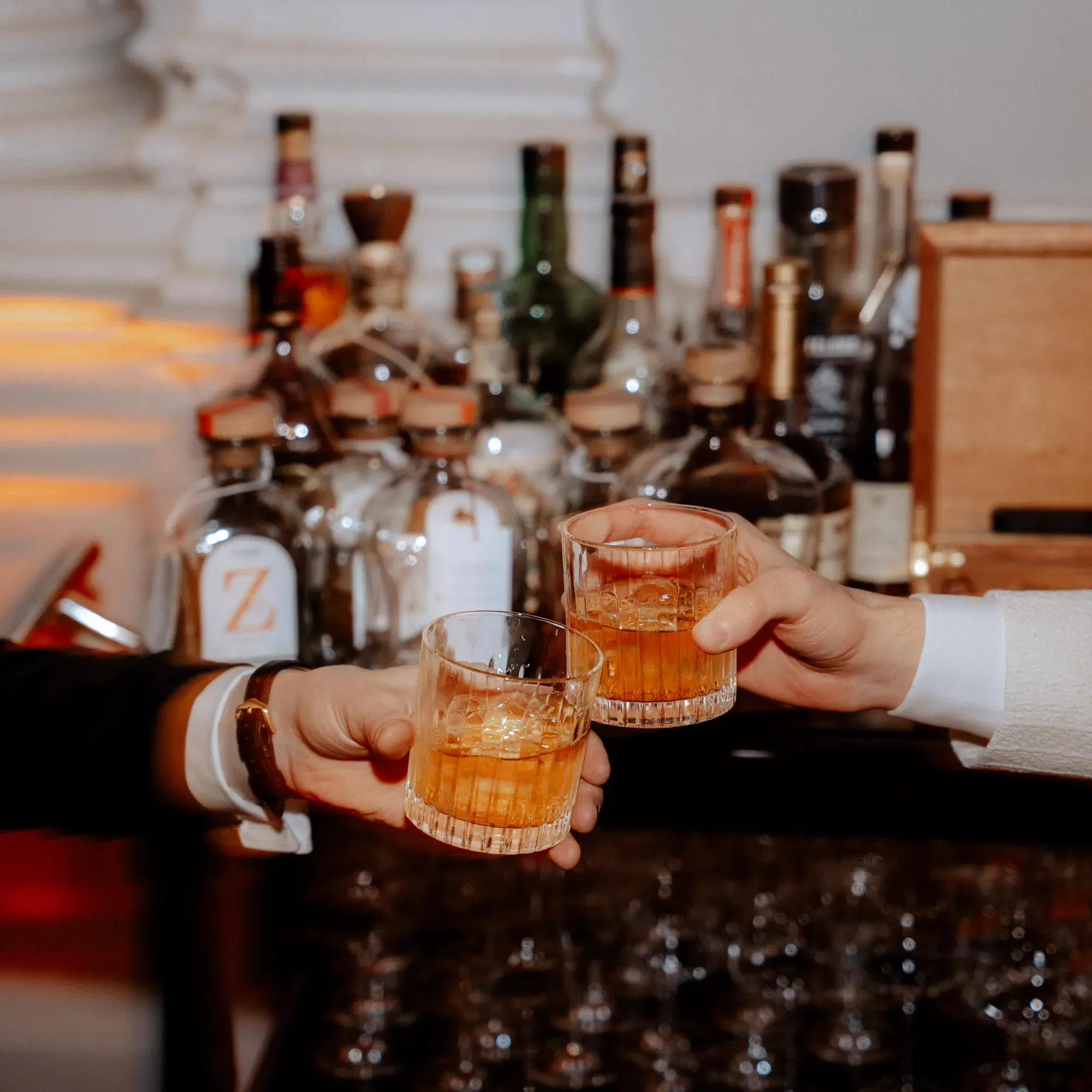 Zwei Männer stoßen mit Drinks an. Es sidn nur ihre Arme zu sehen. Dahinter steht eine mobile Bar.