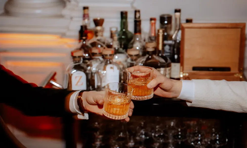 Zwei Männer stoßen mit Drinks an. Es sidn nur ihre Arme zu sehen. Dahinter steht eine mobile Bar.