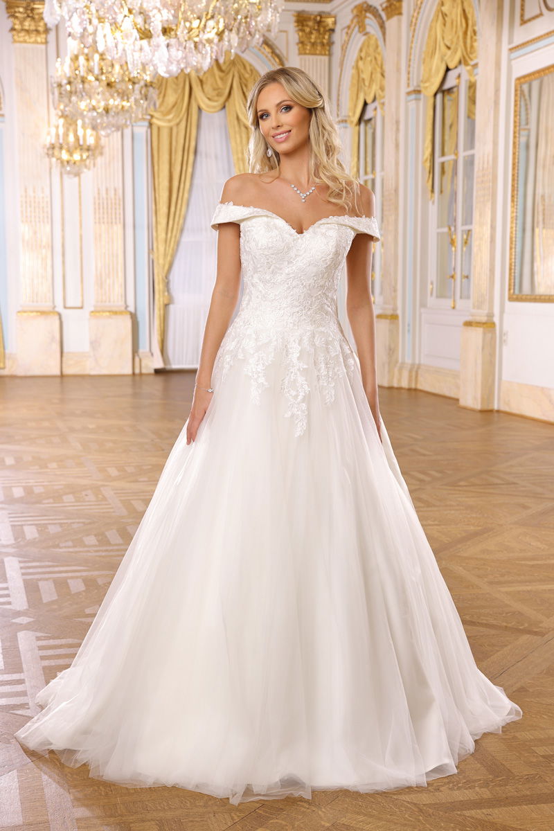 Braut in einem romantischen, schulterfreien Hochzeitskleid mit floralen Details, die in einem prunkvollen Raum mit goldenen Akzenten steht.