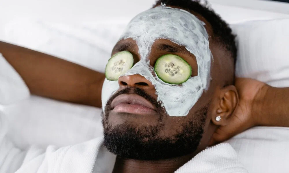 Ein Mann liegt entspannt mit einer Tonerde-Gesichtsmaske und Gurkenscheiben auf den Augen, perfekt für eine beruhigende Spa-Behandlung.