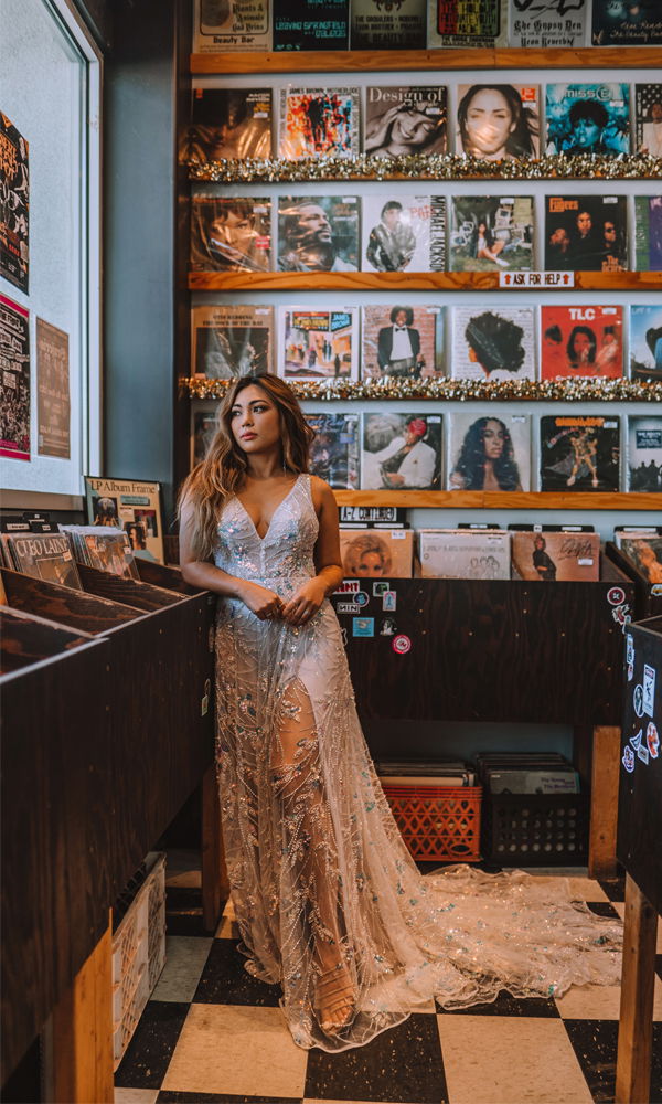 Stilvolle Braut in einem glitzernden Boho-Hochzeitskleid mit tiefem Ausschnitt und funkelnden Details, in einem Schallplattenladen.