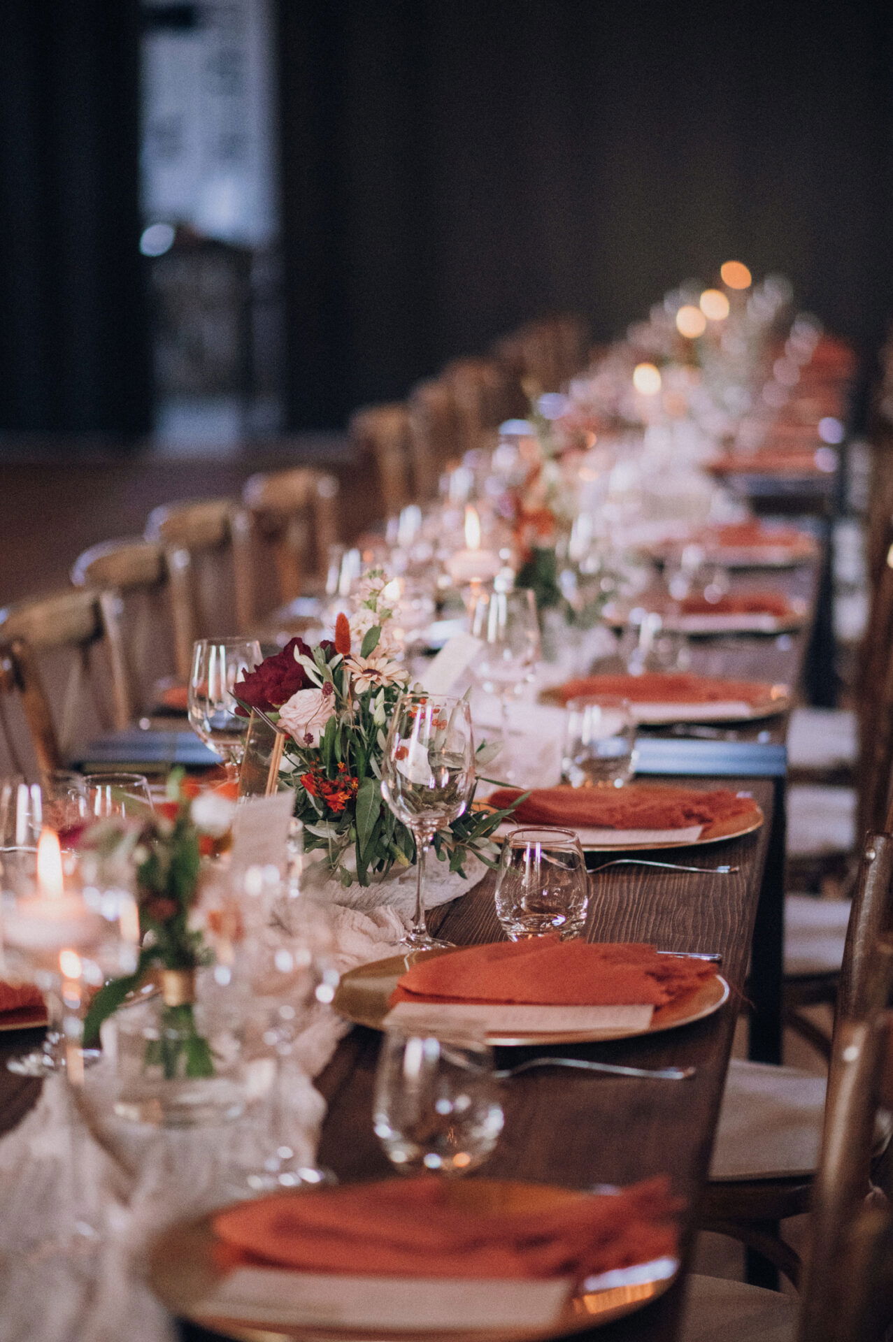 Der gedeckte Hochzeitstisch mit rustikalem Holzdesign und sanften Orangetönen wird durch Blumen und zartes Kerzenlicht romantisch beleuchtet.